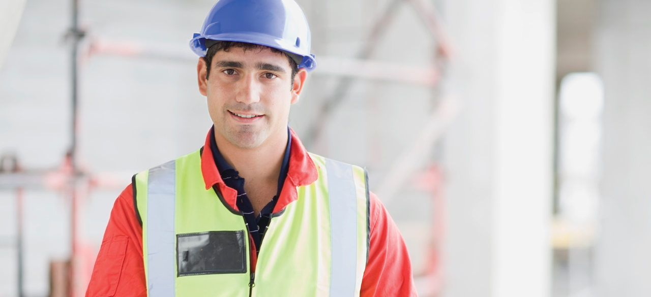 Homme portant un casque de sécurité qui sourit à la caméra avec fond de plan flou