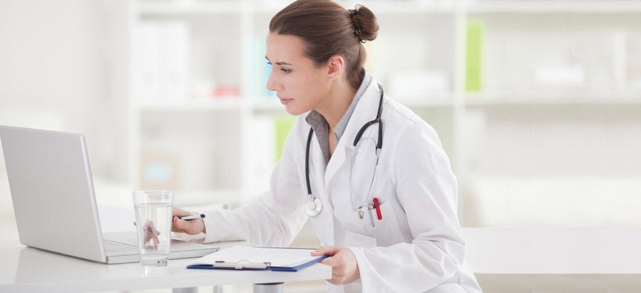 Female doctor sitting at table with a glass of water looking at laptop